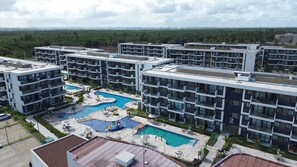 Un moderno complejo hotelero con varias edificaciones, una piscina central y una zona ajardinada.