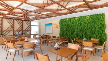 A modern indoor dining area with wooden tables and chairs, a green wall, and a ceiling with wooden beams.