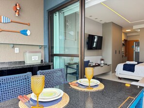 Habitación de hotel con cama, televisor, minibar y zona de estar con mesa y sillones.