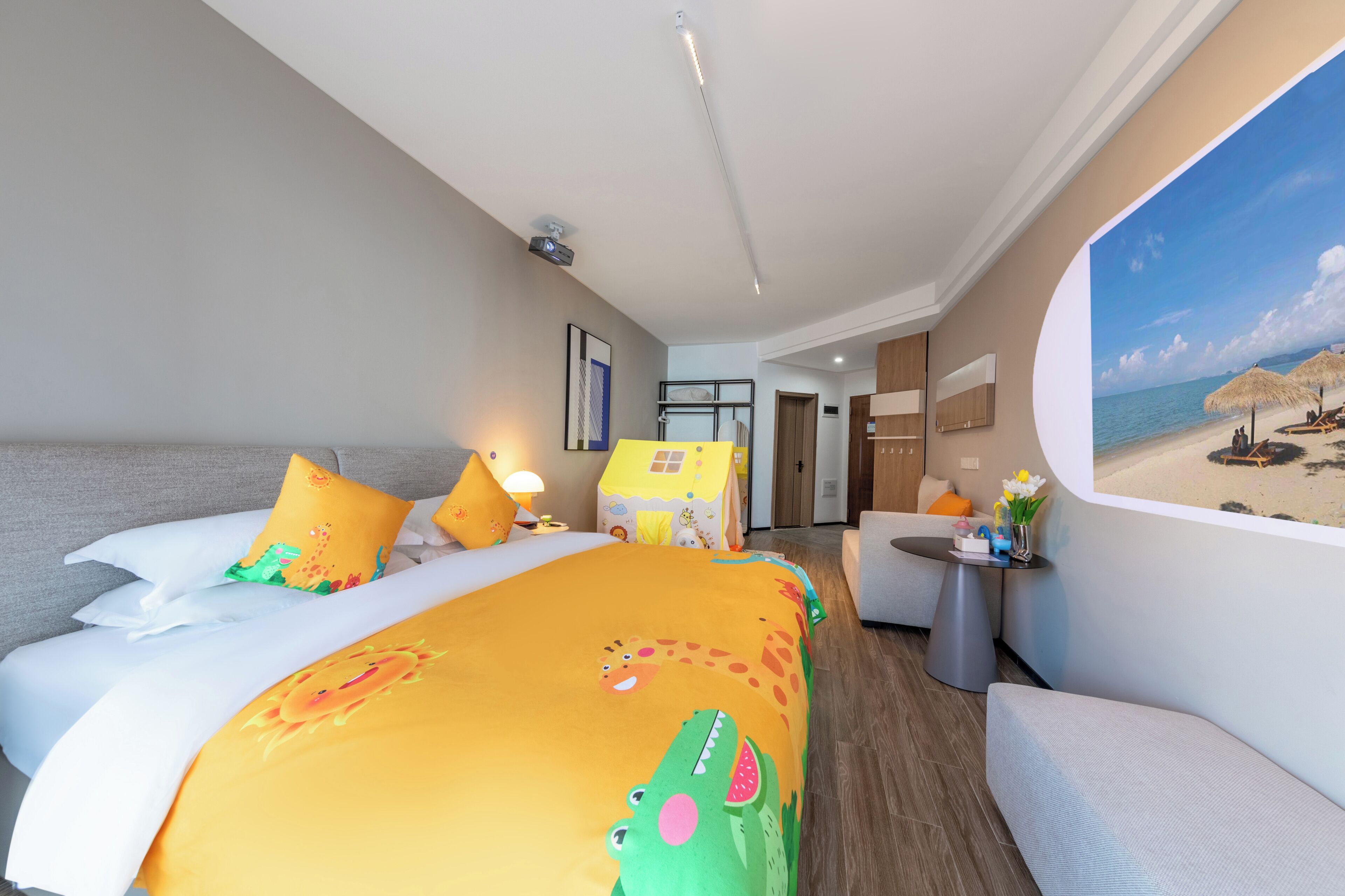 Habitación de hotel con cama, escritorio, silla, mesita de noche, lámpara, un cuadro de playa y una ventana.