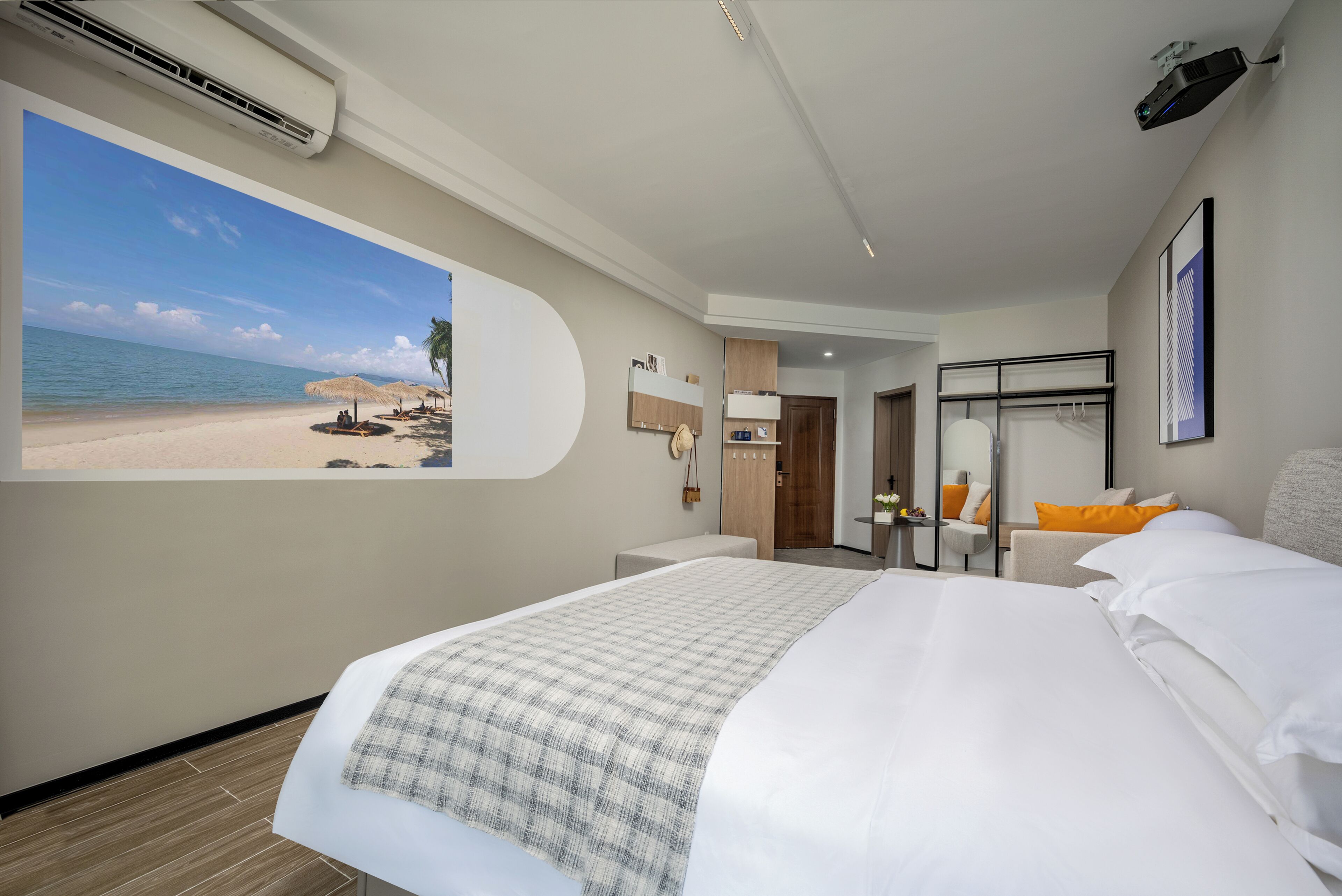 Habitación de hotel con una cama grande, un escritorio, una silla, una mesita, un espejo y un proyector instalado en la pared.