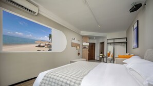 Ein Hotelzimmer mit einem großen Bett, einem Schreibtisch, einem Sessel, einem kleinen Tisch, einem Spiegel und einem an der Wand befestigten Projektor.