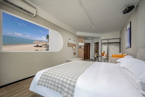 A hotel room with a large bed, a desk, a chair, a small table, a mirror, and a wall-mounted projector.