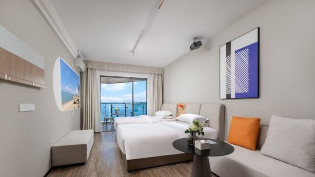Ein Hotelzimmer mit einem großen Bett, einer Couch, einem kleinen Tisch und einem Balkon mit Meerblick.