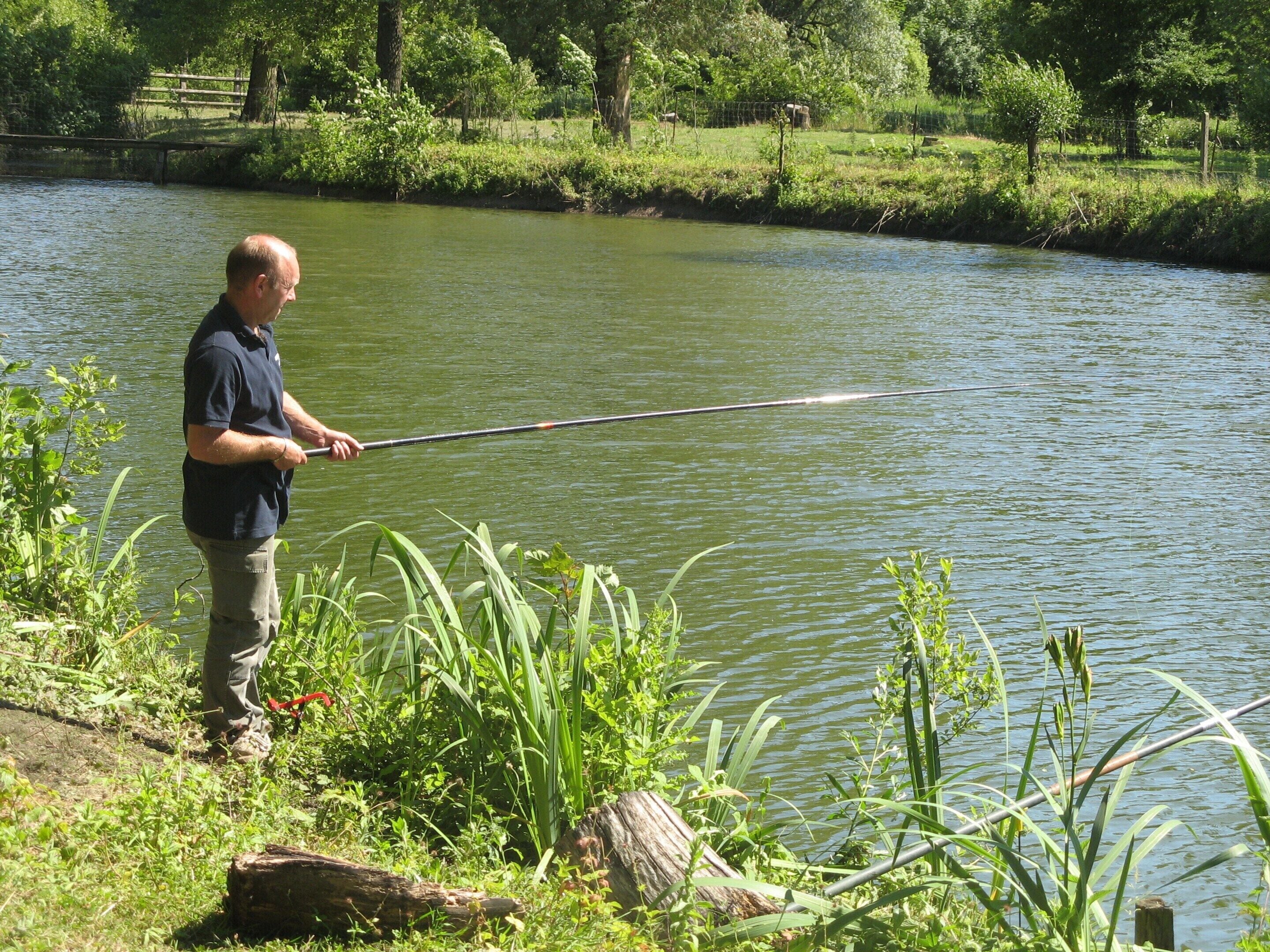 Ein Mann angelt sich etwas an einem ruhigen Fluss, umgeben von viel Grün.