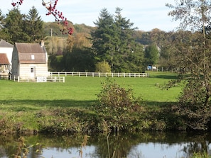 Paisagem rural com um lago, cerca branca e um edifício com telhado vermelho.