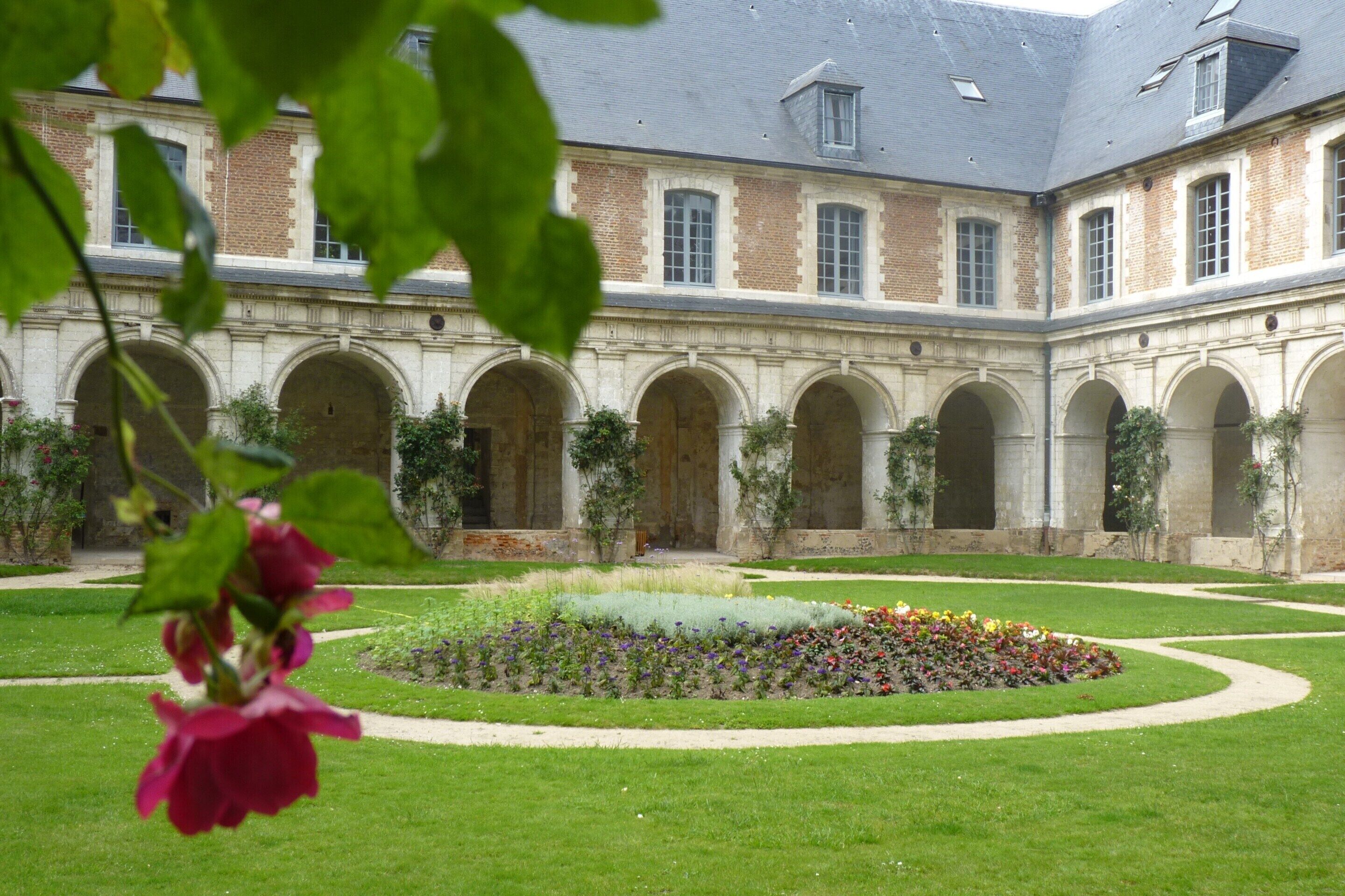 A courtyard with a central garden, surrounded by a building with multiple arches and a brick facade.