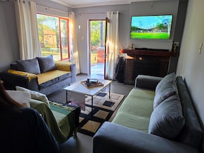 A living room with a sofa, armchair, and a television mounted on the wall. - The Woods at Eleven (Mbombela)