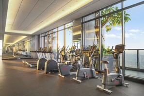 Ein Fitnessstudio mit verschiedenen Trainingsgeräten, großen Fenstern und Blick auf die Stadt.