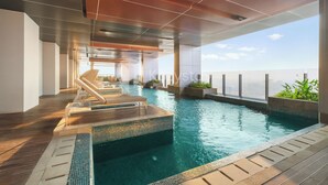 En modern inomhuspool med kristallklart blått vatten, ett trädäck och solstolar.