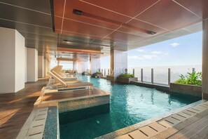 Ein moderner, überdachter Pool mit klarem, blauem Wasser, einer Holzterrasse und Liegestühlen.