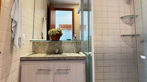 Ein Badezimmer mit einer Granit-Arbeitsplatte, einer Topfpflanze, einem Handtuchhalter und einer Duschkabine aus Glas.