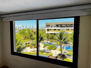 Habitació d'hotel amb una finestra gran que dona a una zona de piscina amb palmeres i un edifici al fons.