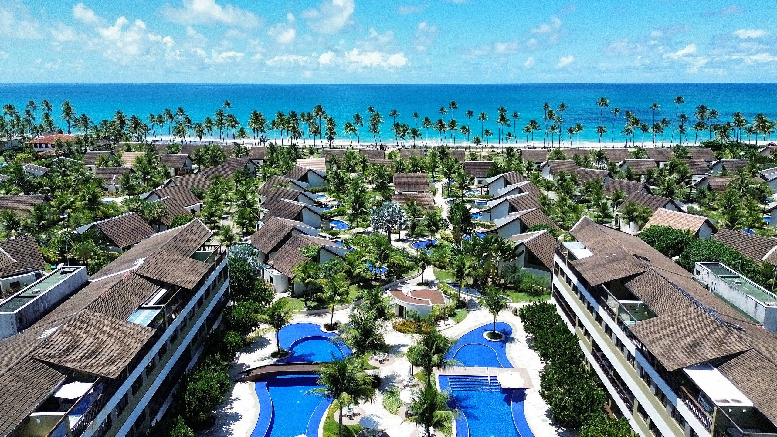 Un resort con varias edificaciones, una piscina central y vista a la playa.