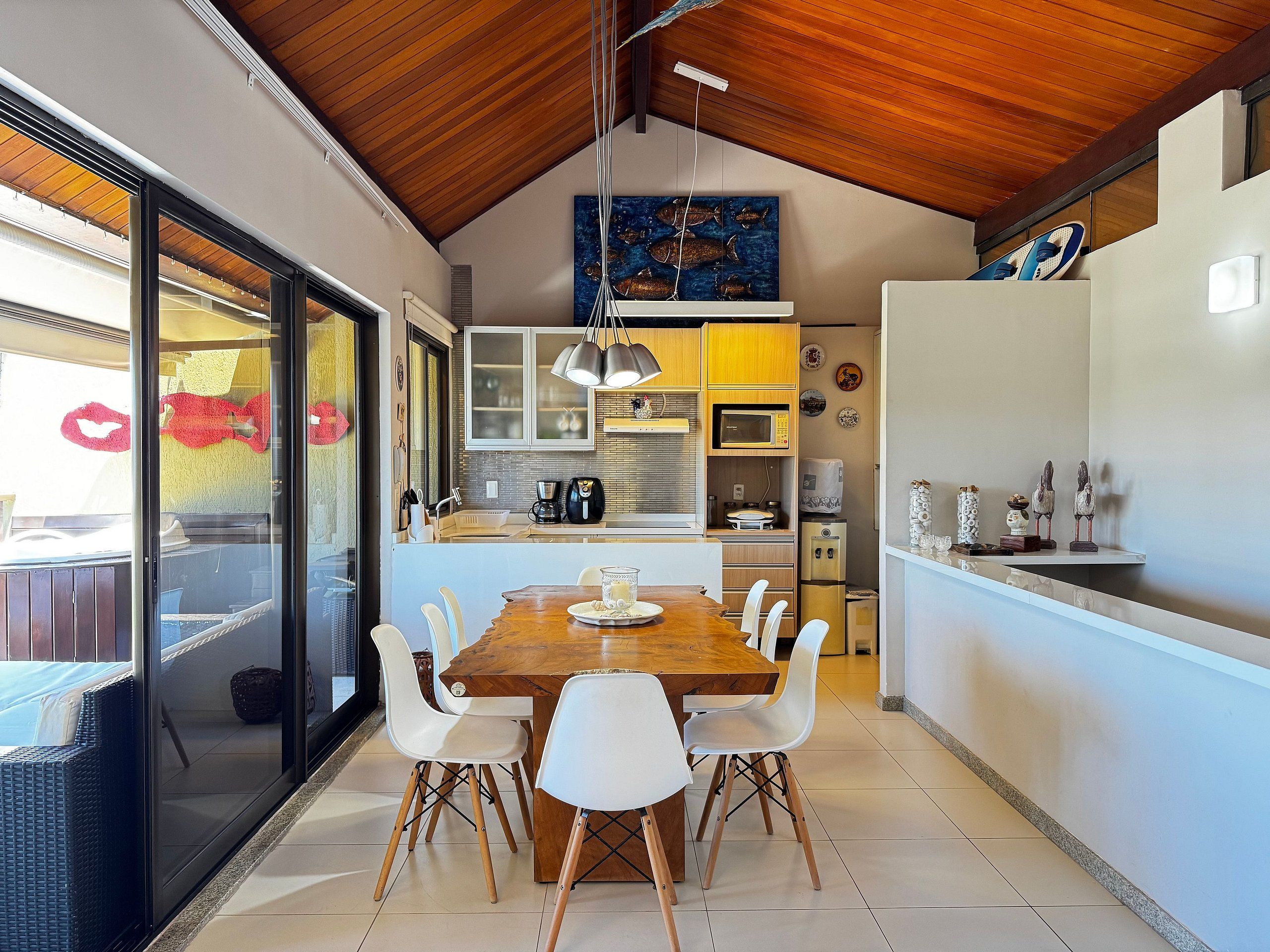 A modern kitchen with a wooden ceiling, a dining table with chairs, and a view through a glass door.