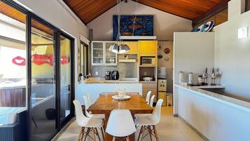 A modern kitchen with a wooden ceiling, a dining table with chairs, and a view through a glass door.
