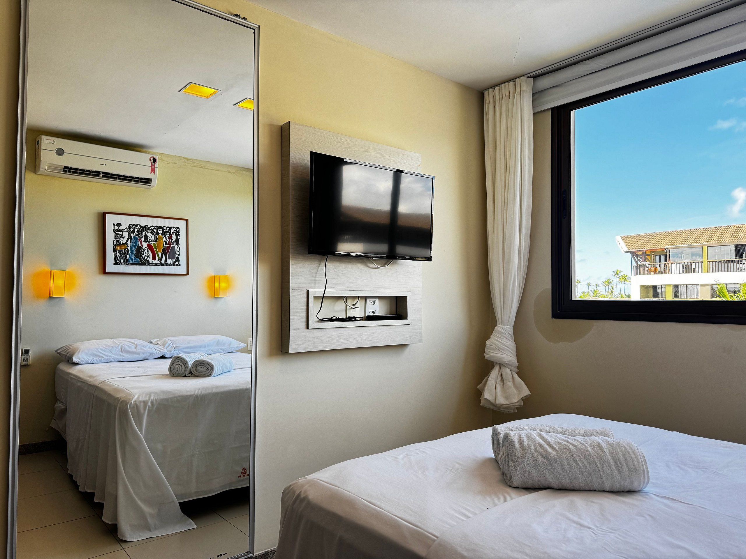 Habitación de hotel con dos camas, televisión, espejo y ventana con vista a edificios.