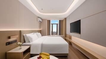 A modern hotel room with a large bed, a flat-screen TV, a bedside table with a vase of flowers, and a view of the city through the window.