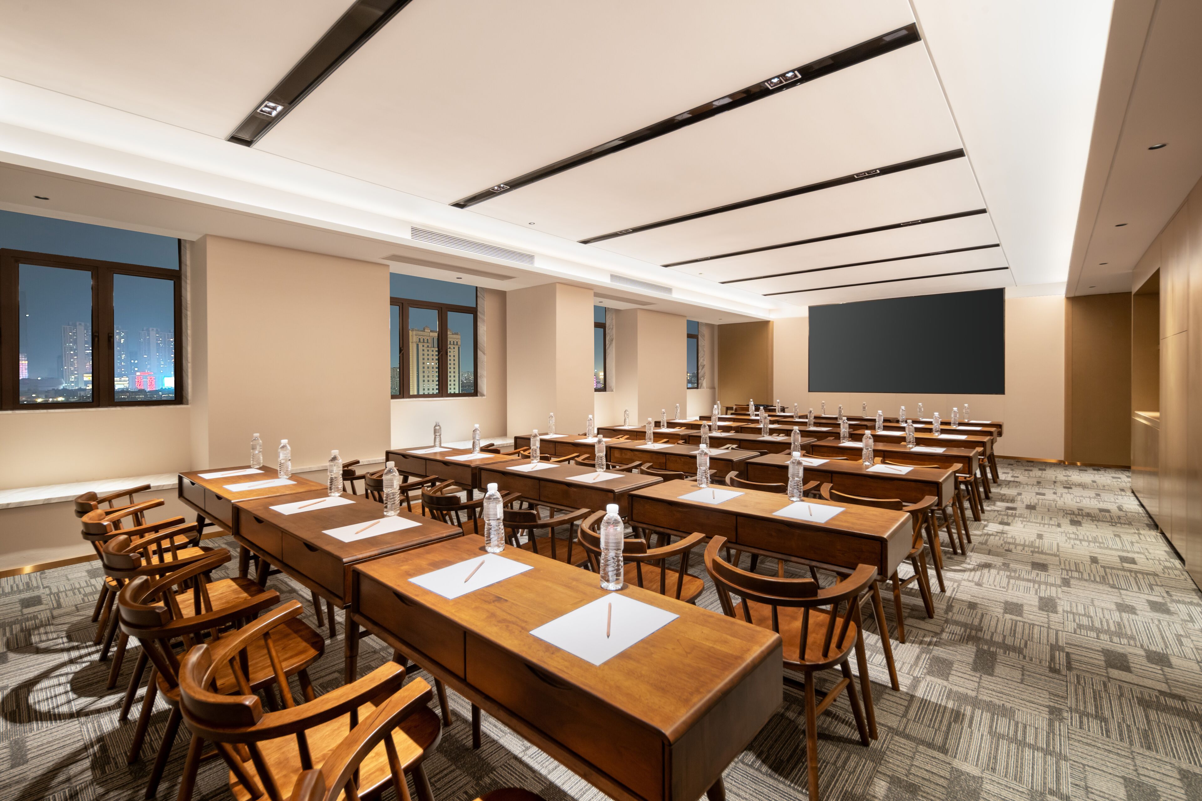 A conference room with multiple tables, chairs, and a large screen for presentations.