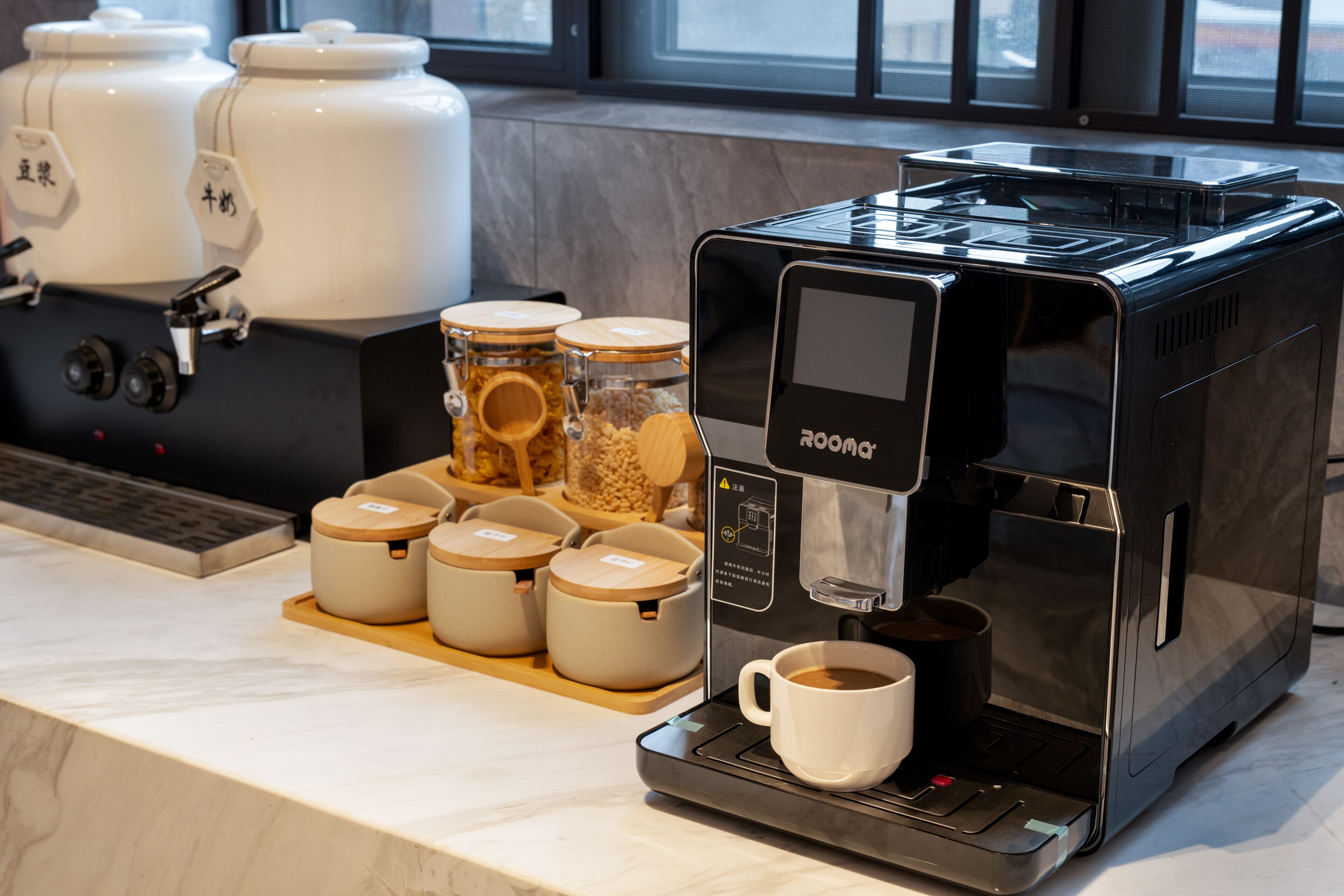 Una cafetera con una taza de café, una bandeja con tazas y recipientes con granos de café.