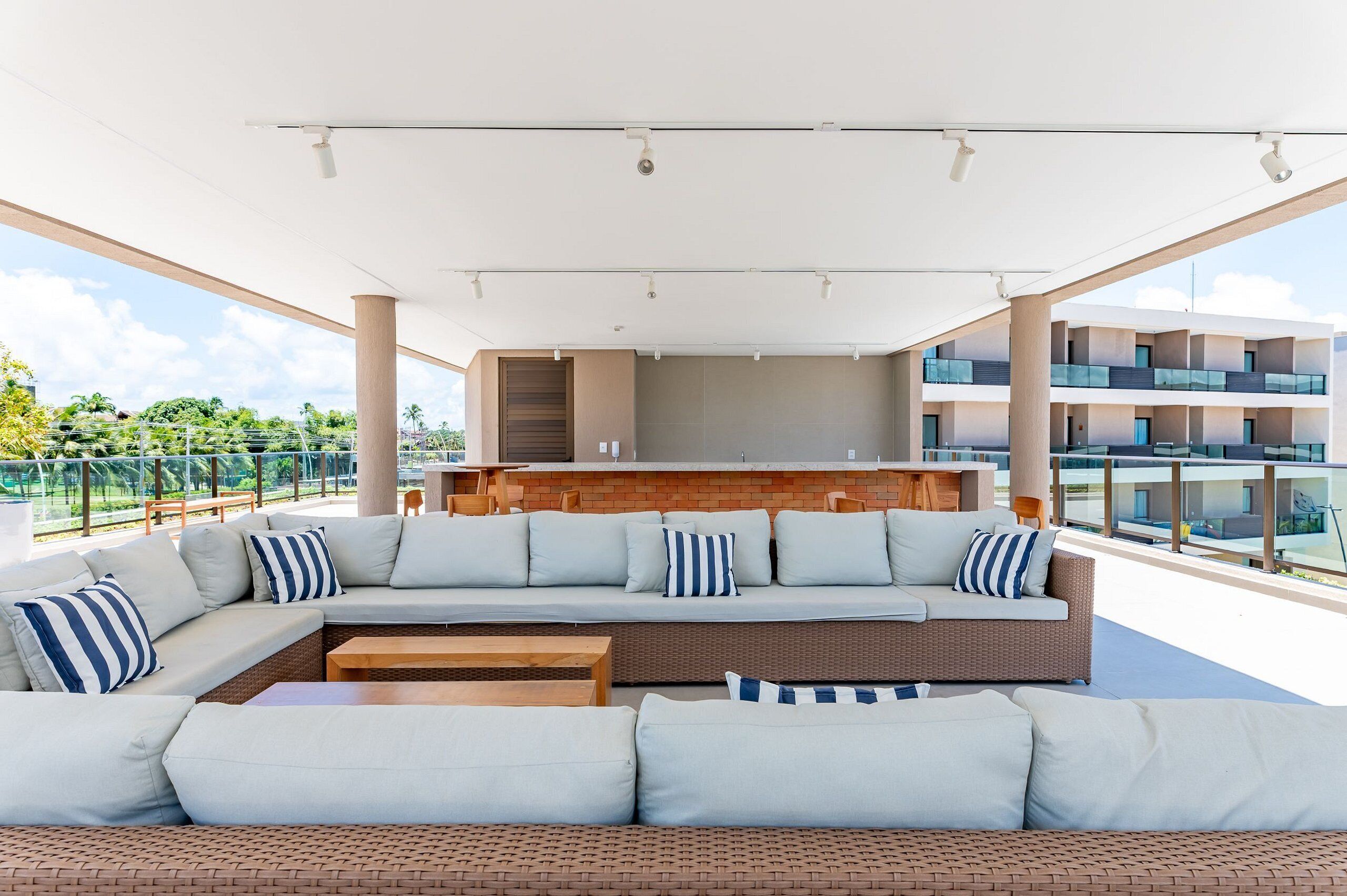 A modern outdoor seating area with a sofa and a coffee table, a kitchen area with a brick backsplash, and a view of a residential building.