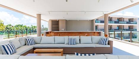 A modern outdoor seating area with a sofa and a coffee table, a kitchen area with a brick backsplash, and a view of a residential building.