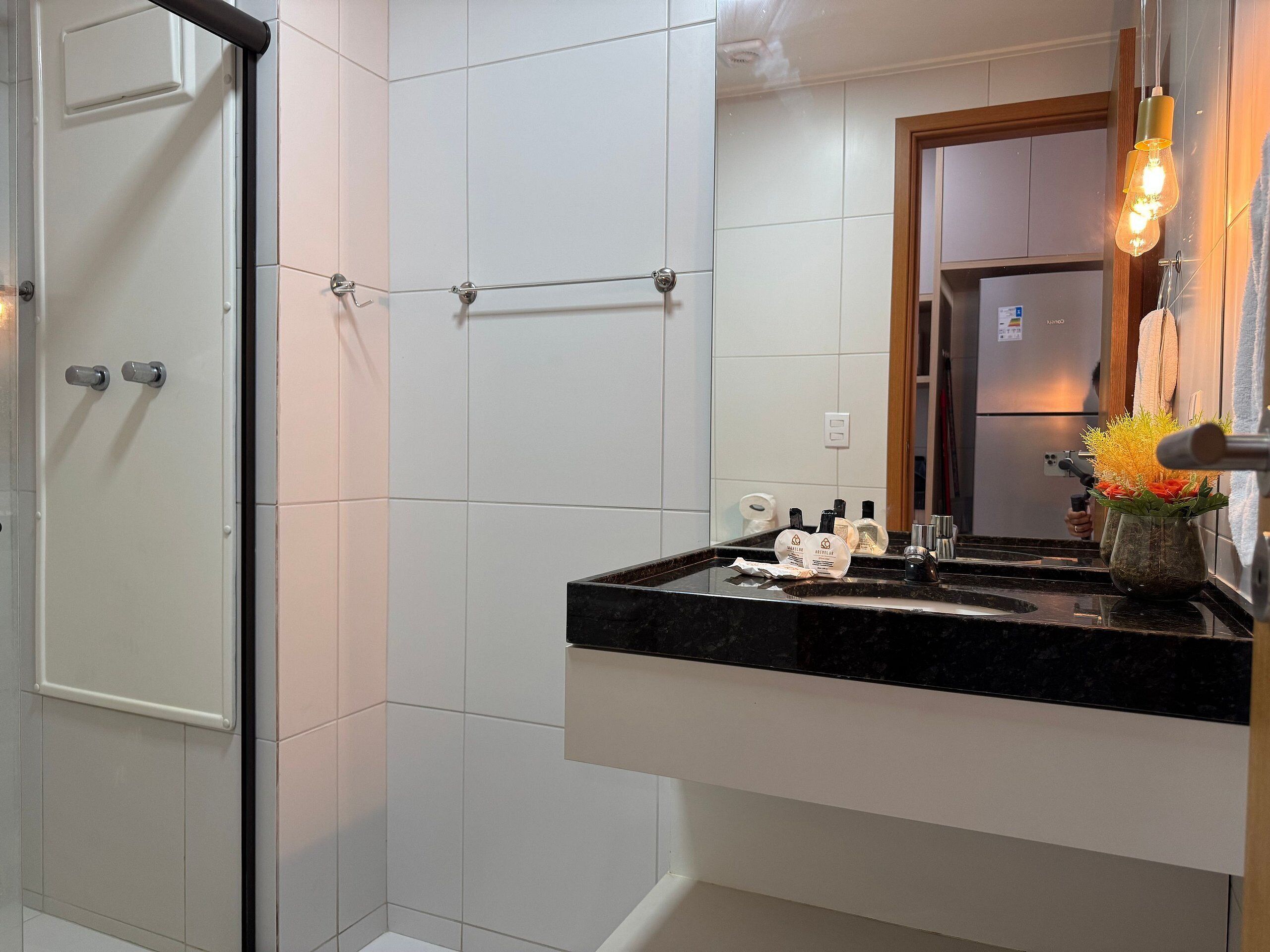 Un baño con azulejos blancos, encimera negra, un espejo y una lámpara colgante.
