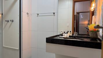 Un baño con azulejos blancos, encimera negra, un espejo y una lámpara colgante.