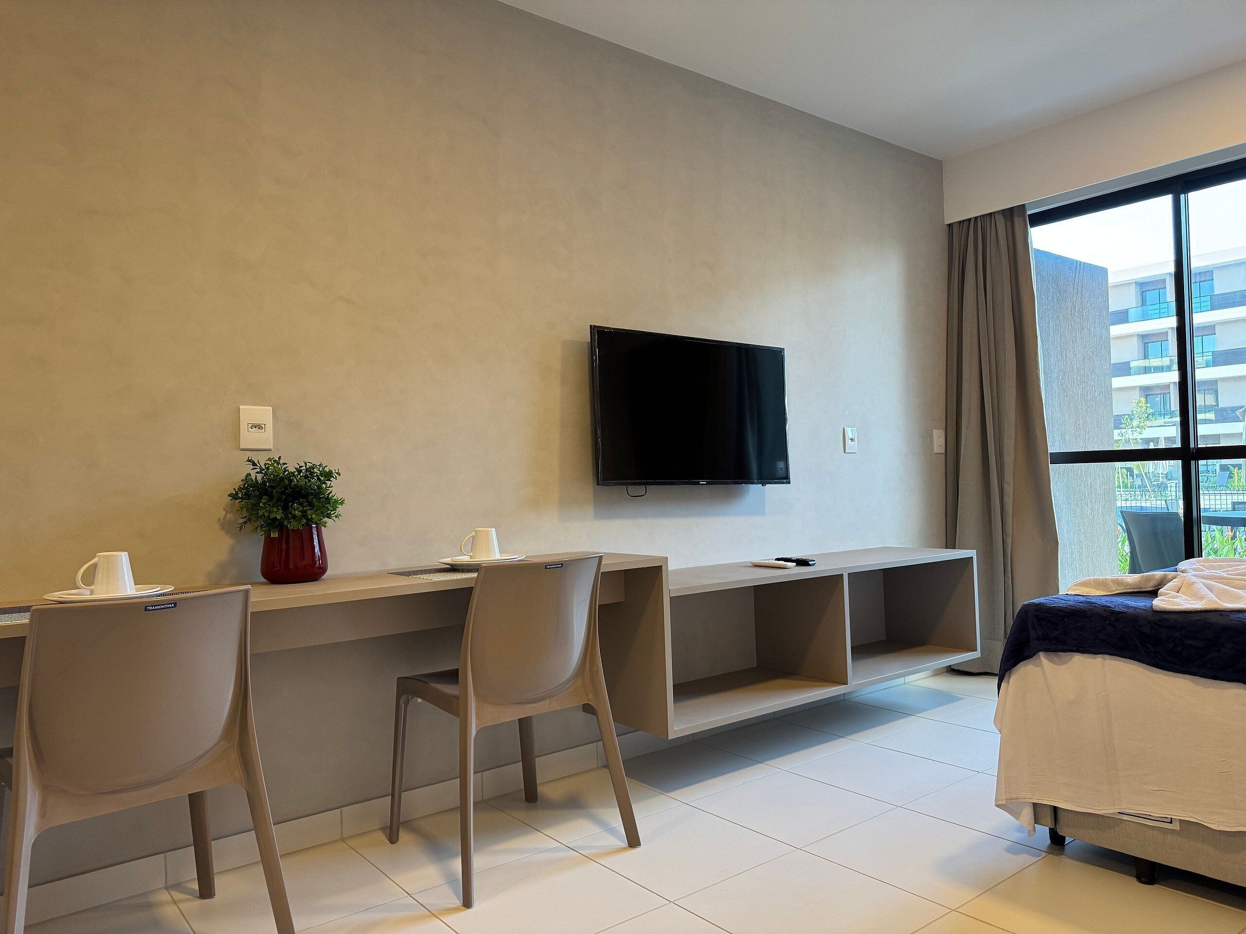 A hotel room with a bed, a desk with a chair, a television, and a large window.