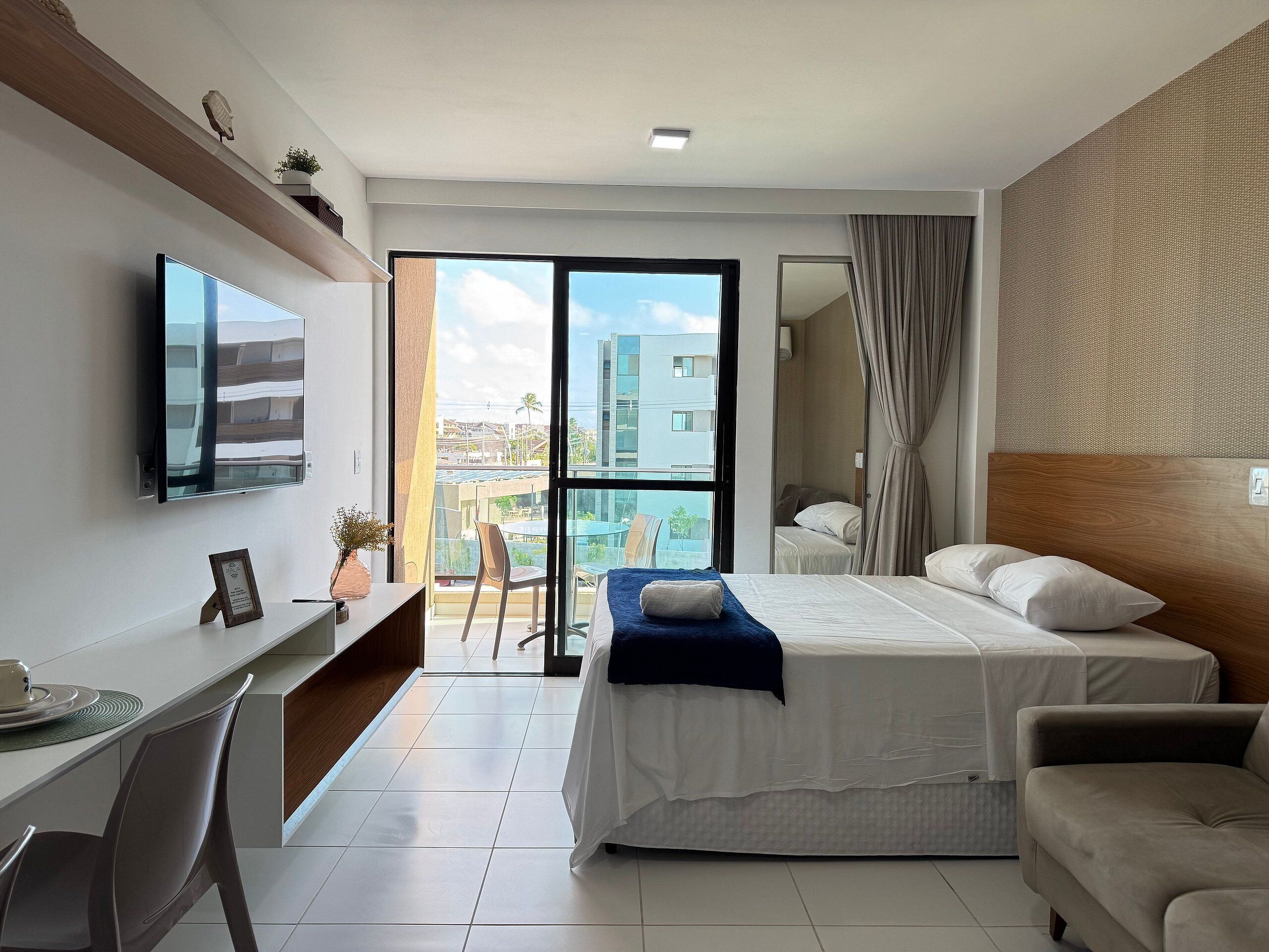 Een moderne hotelkamer met een bed, een bureau, een stoel, een televisie en een balkon met uitzicht op de stad.