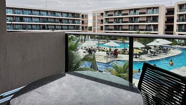 Een hotelbalkon met uitzicht op een zwembad met ligbedden en parasols, en een meer verdwenen gebouw op de achtergrond.