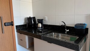 Een keuken met een zwart aanrecht, een koffiezetapparaat, een spoelbak en een prullenbak.
