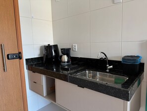 Eine Küche mit schwarzem Arbeitsplatz, einer Kaffeemaschine, einem Spülbecken und einem Mülleimer.