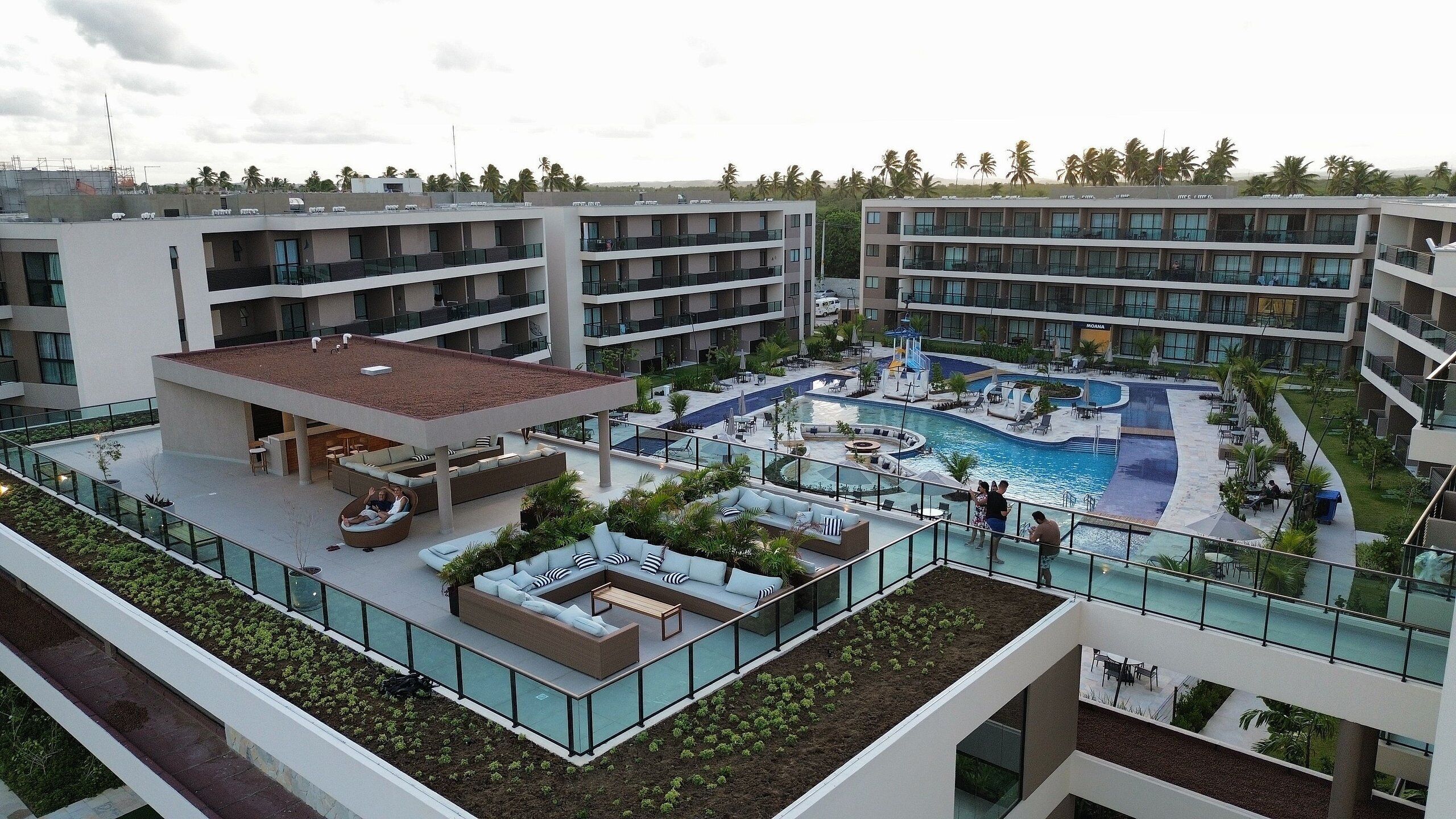 Un hotel de varios pisos con piscina en la azotea, zona de estar al aire libre y jardín ajardinado.