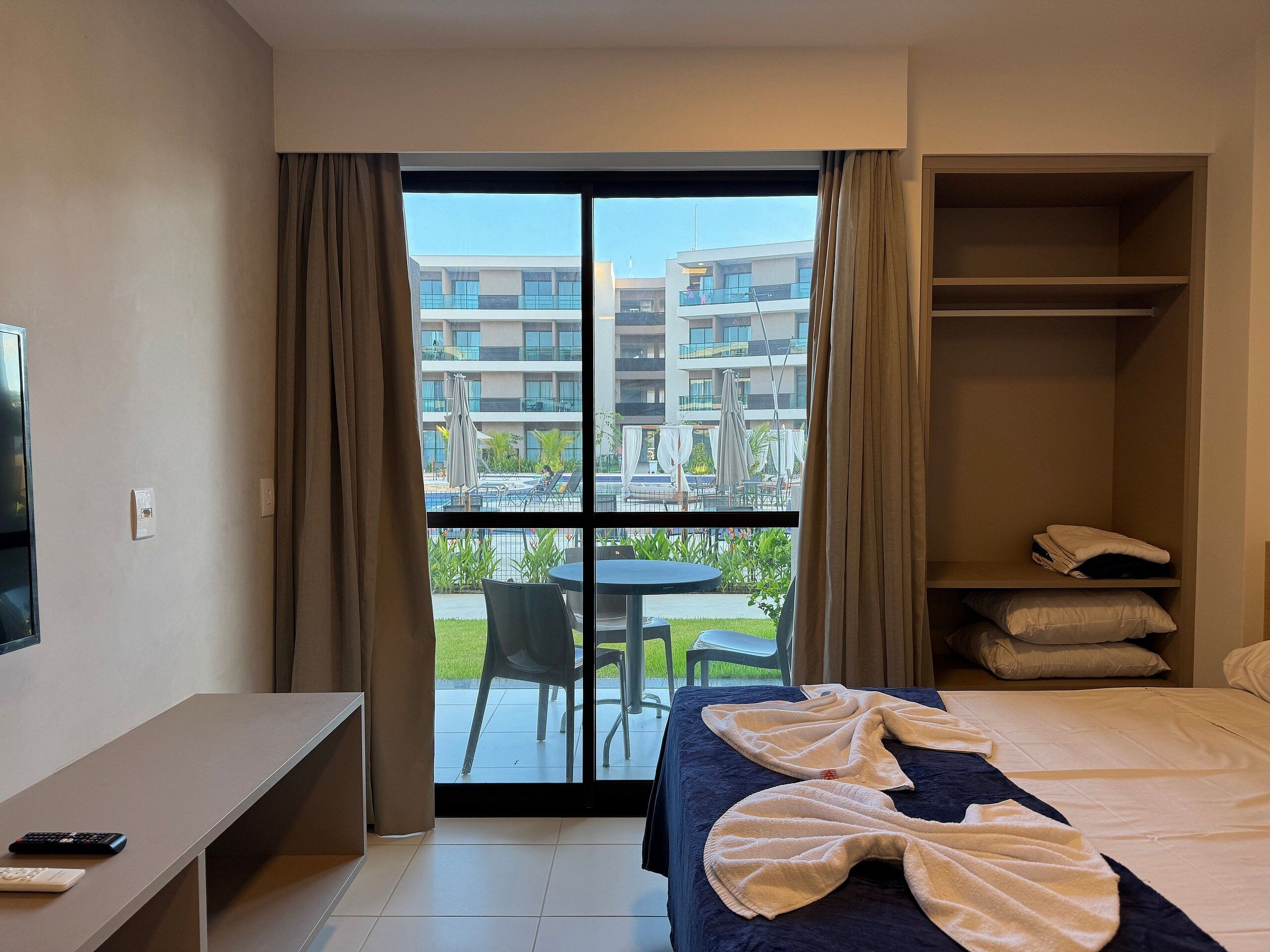 Ein Hotelzimmer mit einem Bett, einem Schreibtisch, einem Stuhl und Blick auf einen Pool und Gebäude.