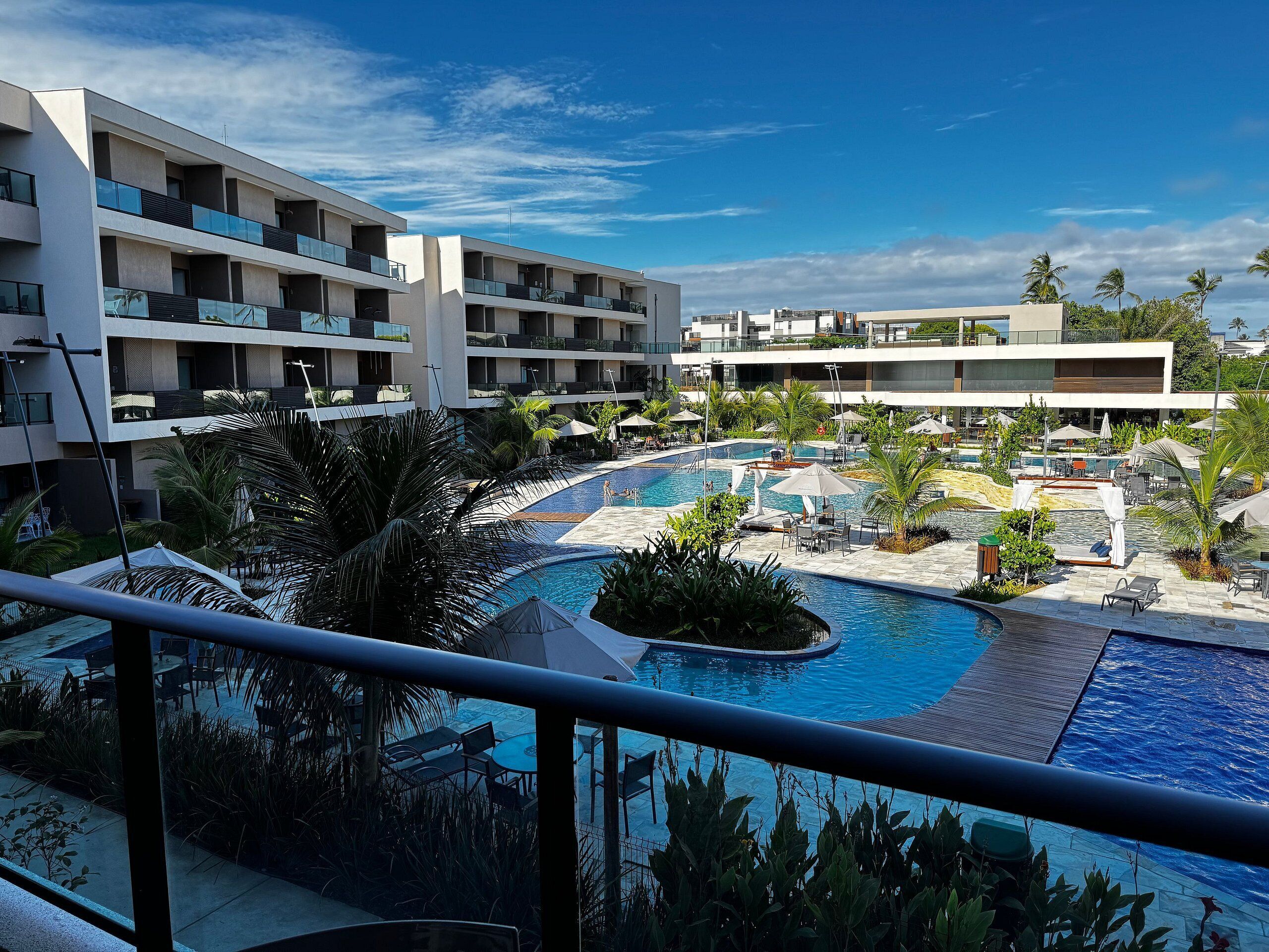 A hotel with a swimming pool, outdoor seating, and palm trees.