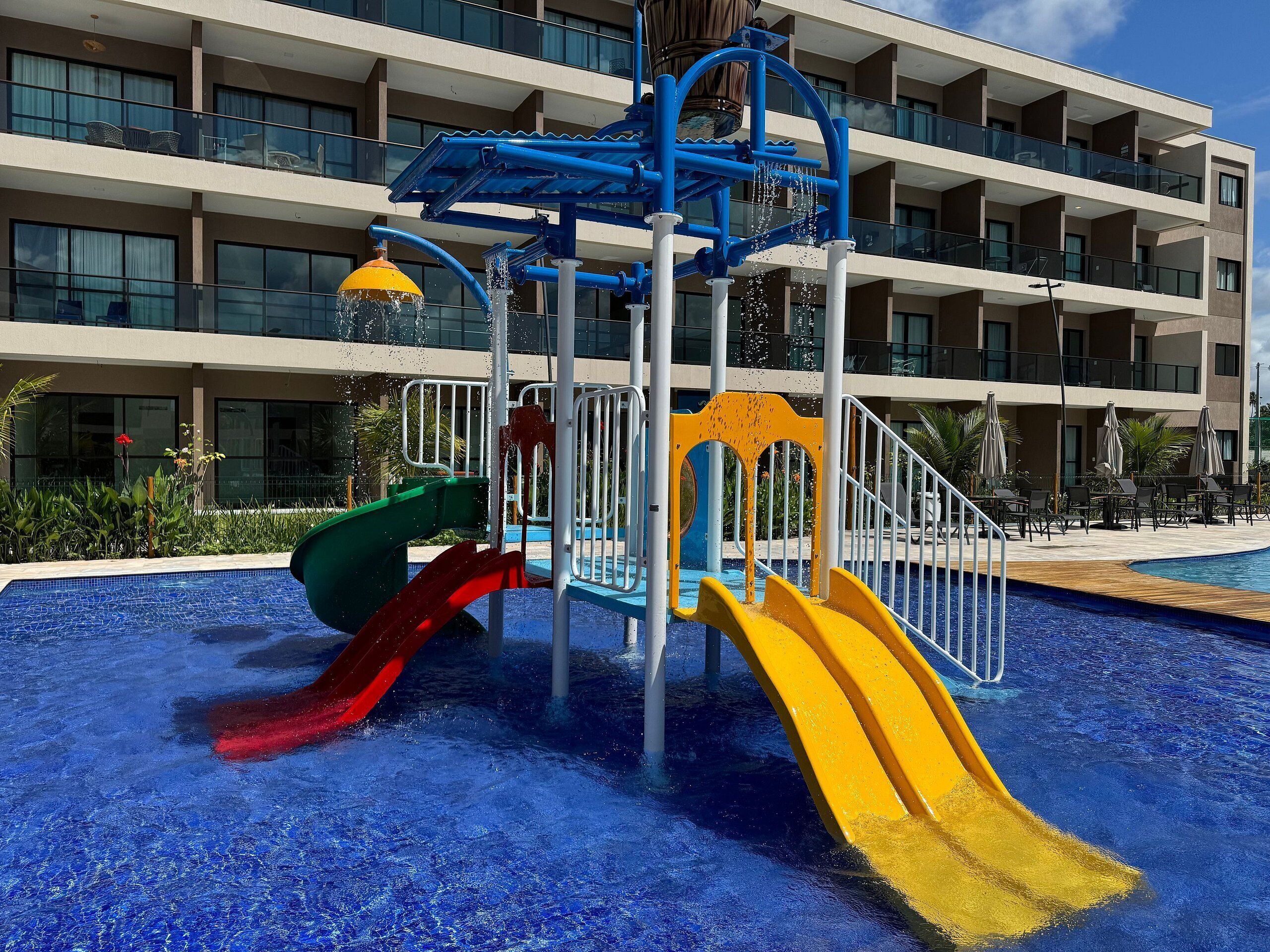 Un parc aquatique avec des toboggans et une piscine, entouré d’un immeuble à plusieurs étages doté de balcons.
