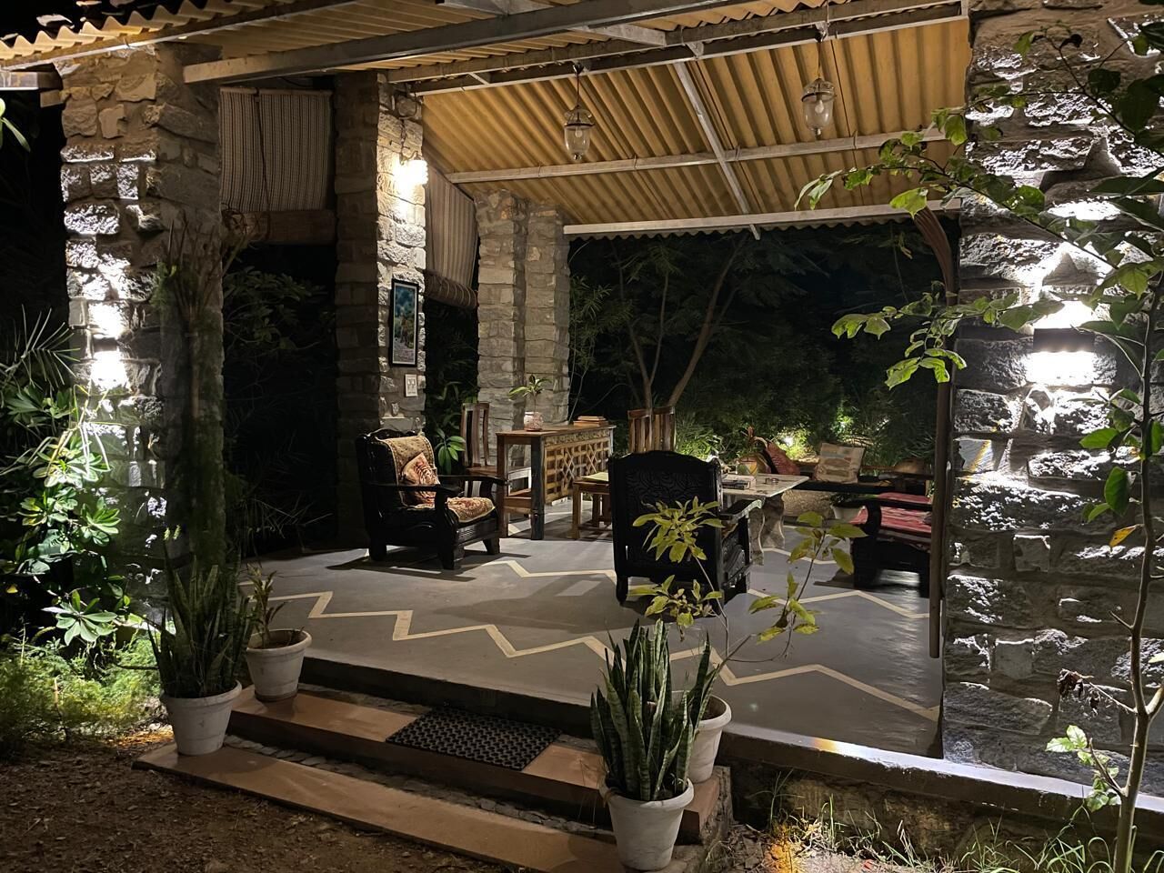 An outdoor seating area with stone walls, potted plants, and a patterned floor.