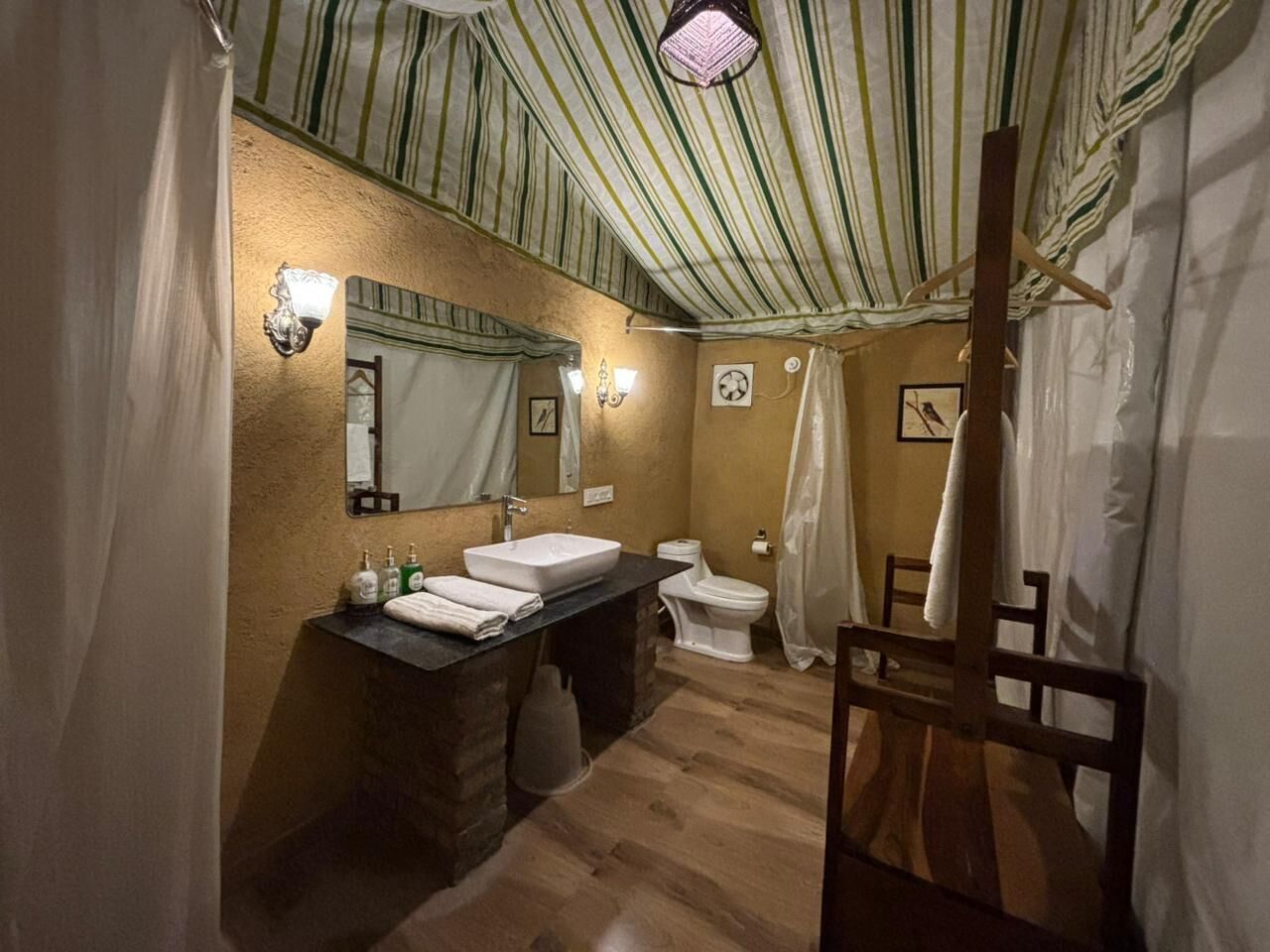 A bathroom with a striped ceiling, a sink, a toilet, and a shower curtain.