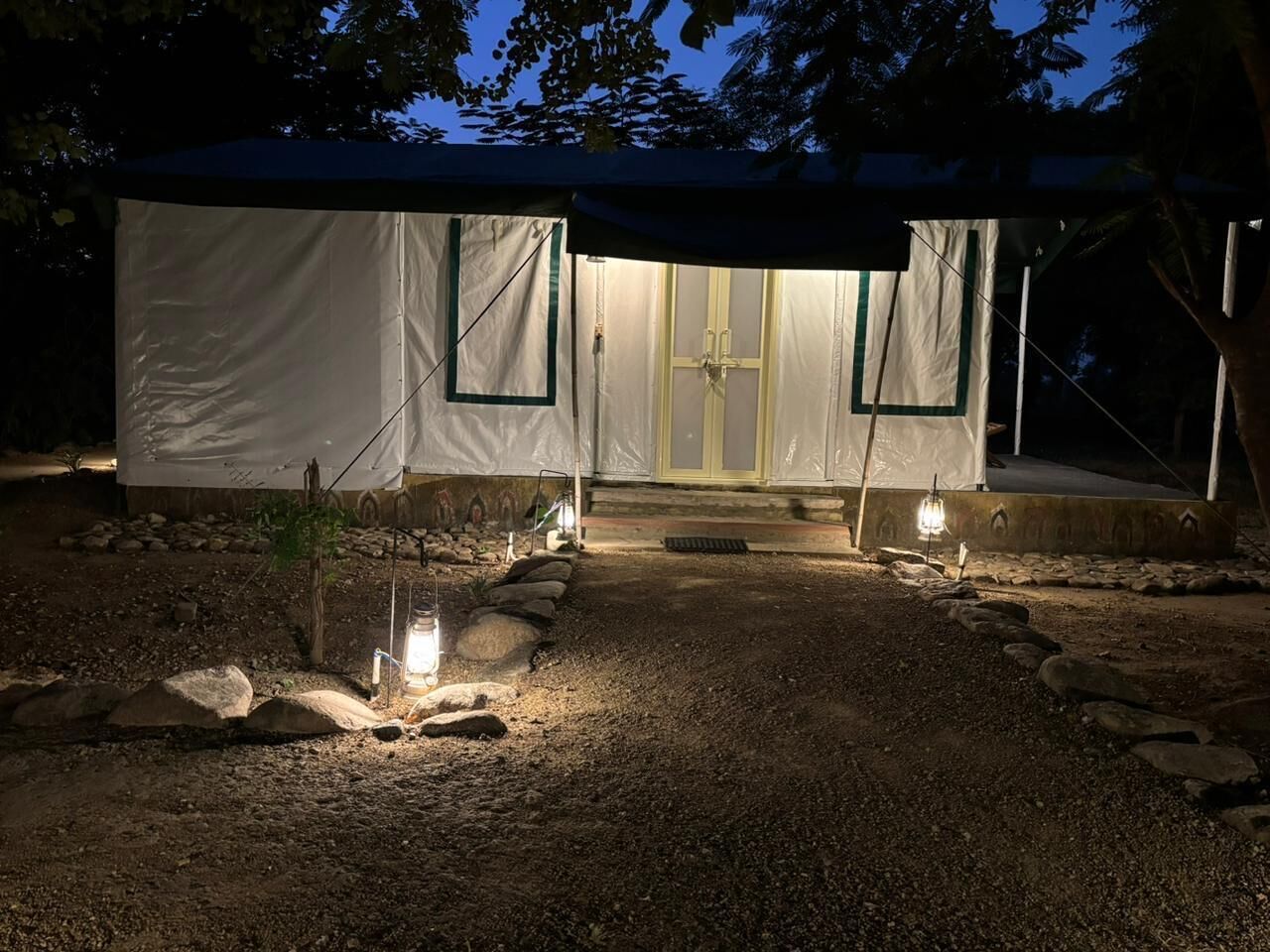 A tented structure with a gravel path leading to a door, surrounded by rocks and minimal vegetation.