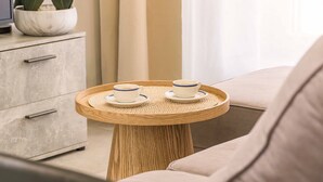 A modern room with a round wooden table, two cups on saucers, a sofa, a cabinet, and a potted plant. - Apartment Le Cèdre  by Sur la mer (Le Muy)