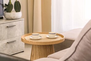Ein modernes Zimmer mit einem runden Holztisch, zwei Tassen auf Untertellern, einem Sofa, einem Schrank und einer Topfpflanze.