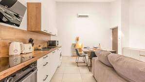 A modern kitchen with a built-in oven, microwave, and coffee maker. There is a dining area with a table set for two and a sofa. - Apartment Le Cèdre  by Sur la mer (Le Muy)