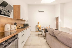 Eine moderne Küche mit Backofen, Mikrowelle und Kaffeemaschine. Es gibt einen Essbereich mit Tisch für zwei Personen und eine Couch.
