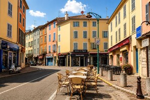 Eine Straße mit Cafés und Geschäften, Außenbereich zum Sitzen und blauem Himmel.