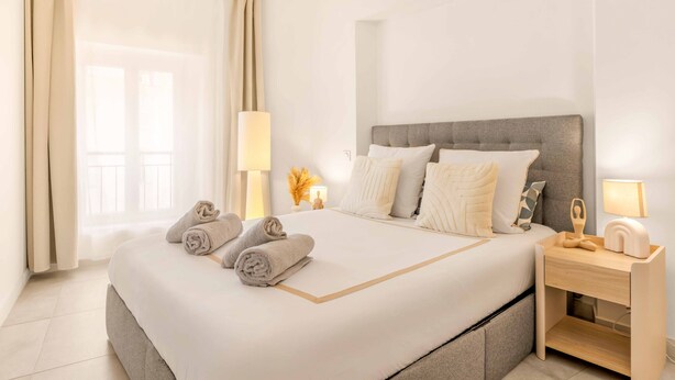 A hotel room with a large bed, a bedside table with a lamp, and a view of the outdoors through the window. - Apartment Le Cèdre  by Sur la mer (Le Muy)