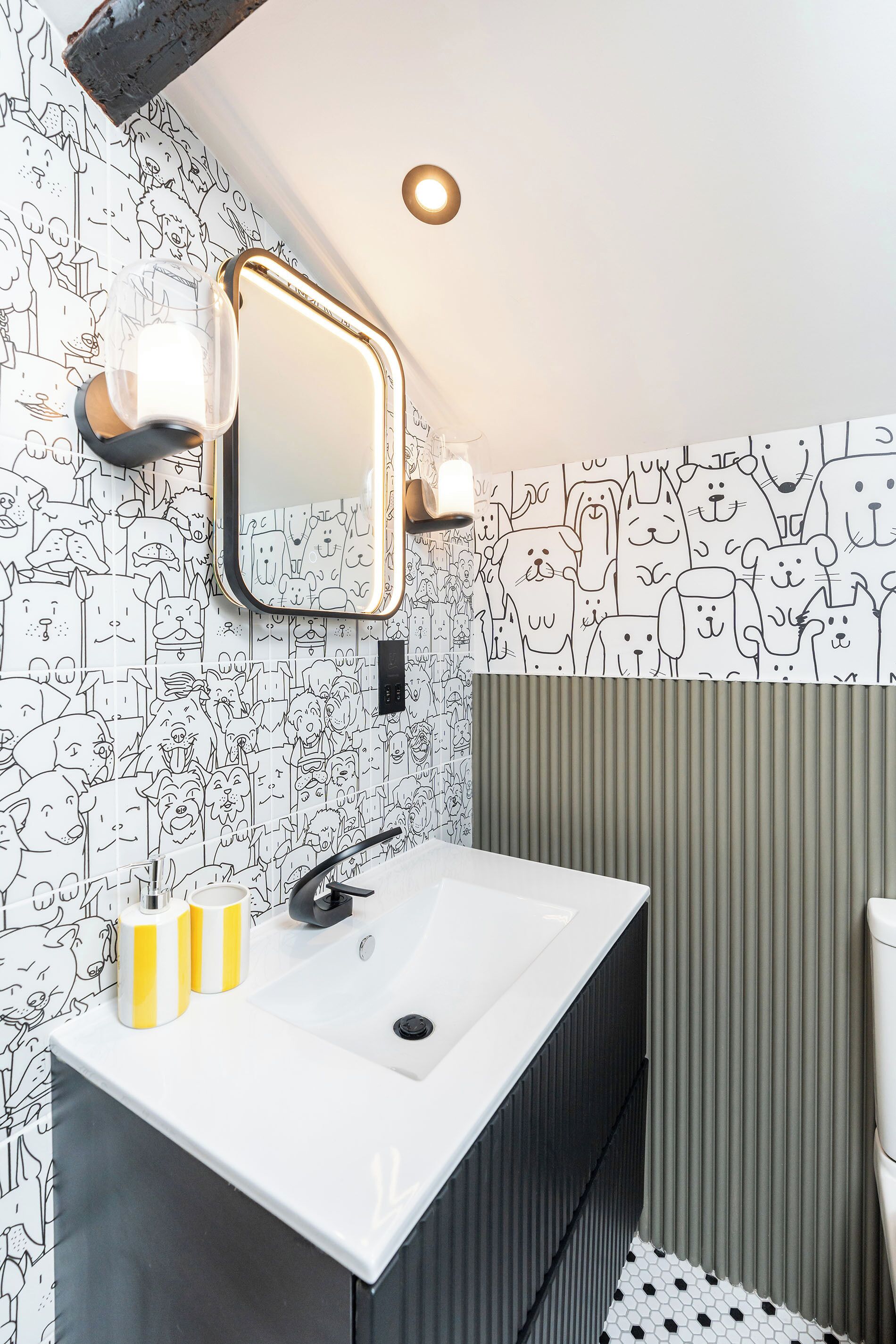 A bathroom with a white sink, a mirror with lights, and a wall with cartoon animal drawings.
