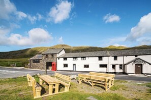 A traditional stone and white building with a red door, benches, and a clear view of the surrounding landscape. - Kirkstone Pass Mountain Rooms (Windermere)