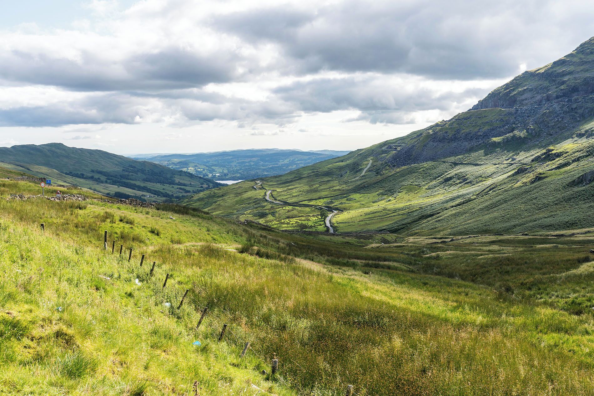 Un paysage rural caractérisé par des collines douces, une route sinueuse et un mur de pierres.