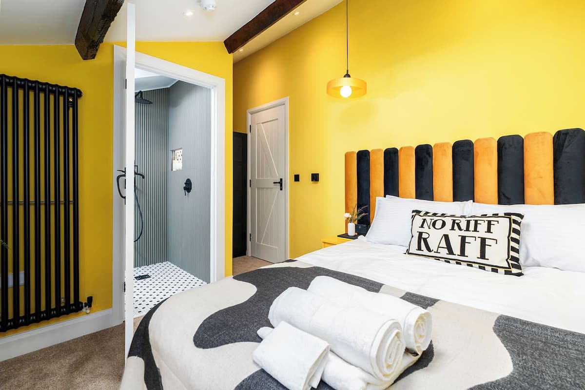 A hotel room with a bed, a headboard with alternating black and orange cushions, a bedside table with a lamp, and a towel on the bed.
